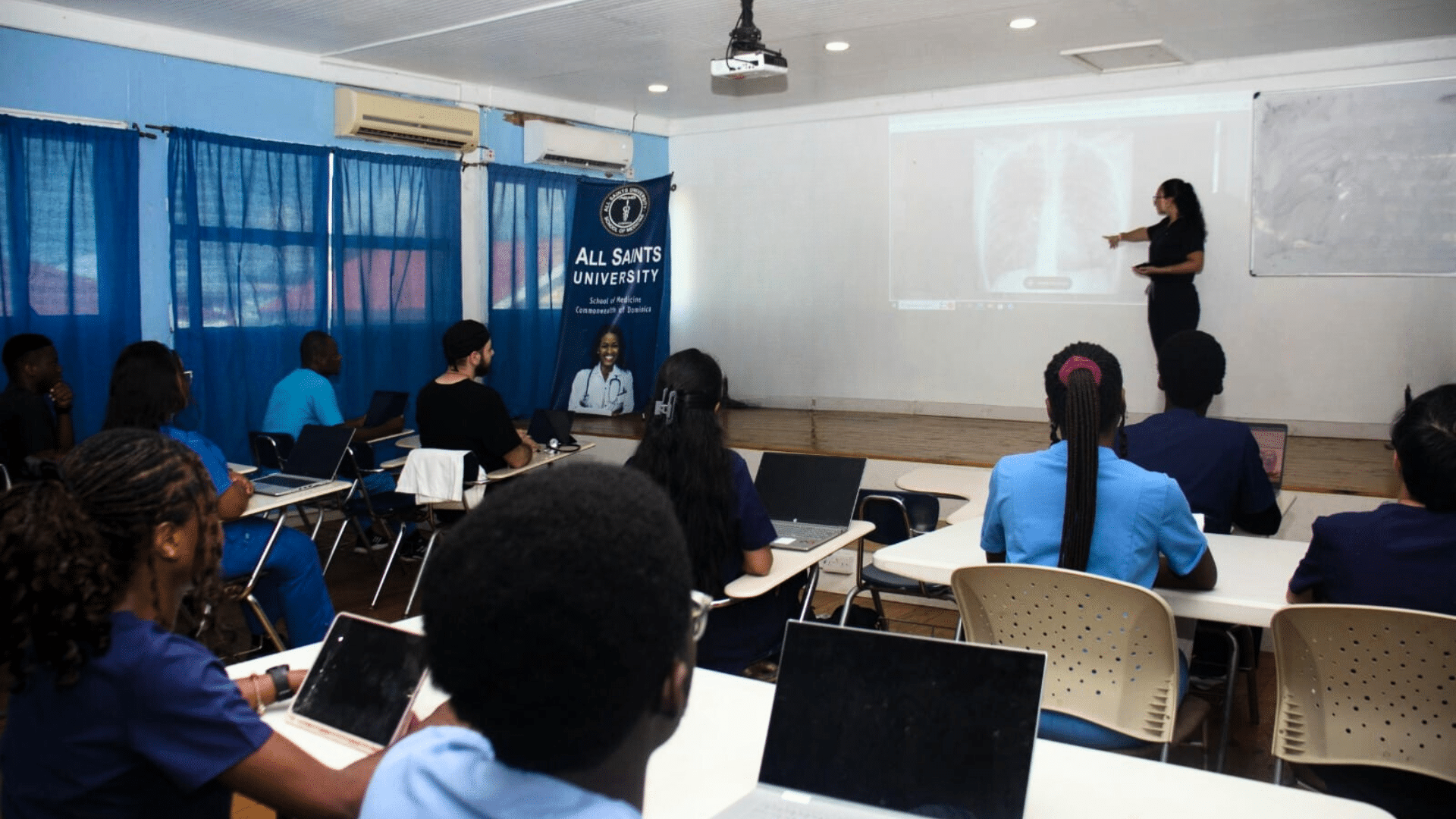 All Saints University students seated in a classroom attentively listening to a professor during a lecture.